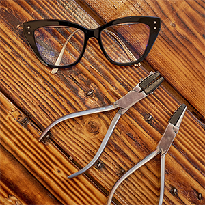 To tænger til reperation af briller, ligger på et bord sammen med et brillestel. Bordet af træ. Få briller jsuteret og repereret hos Sandberg Optik.