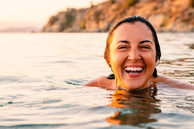 kvinde der griner og svømmer i havet med kontaltlinser på.